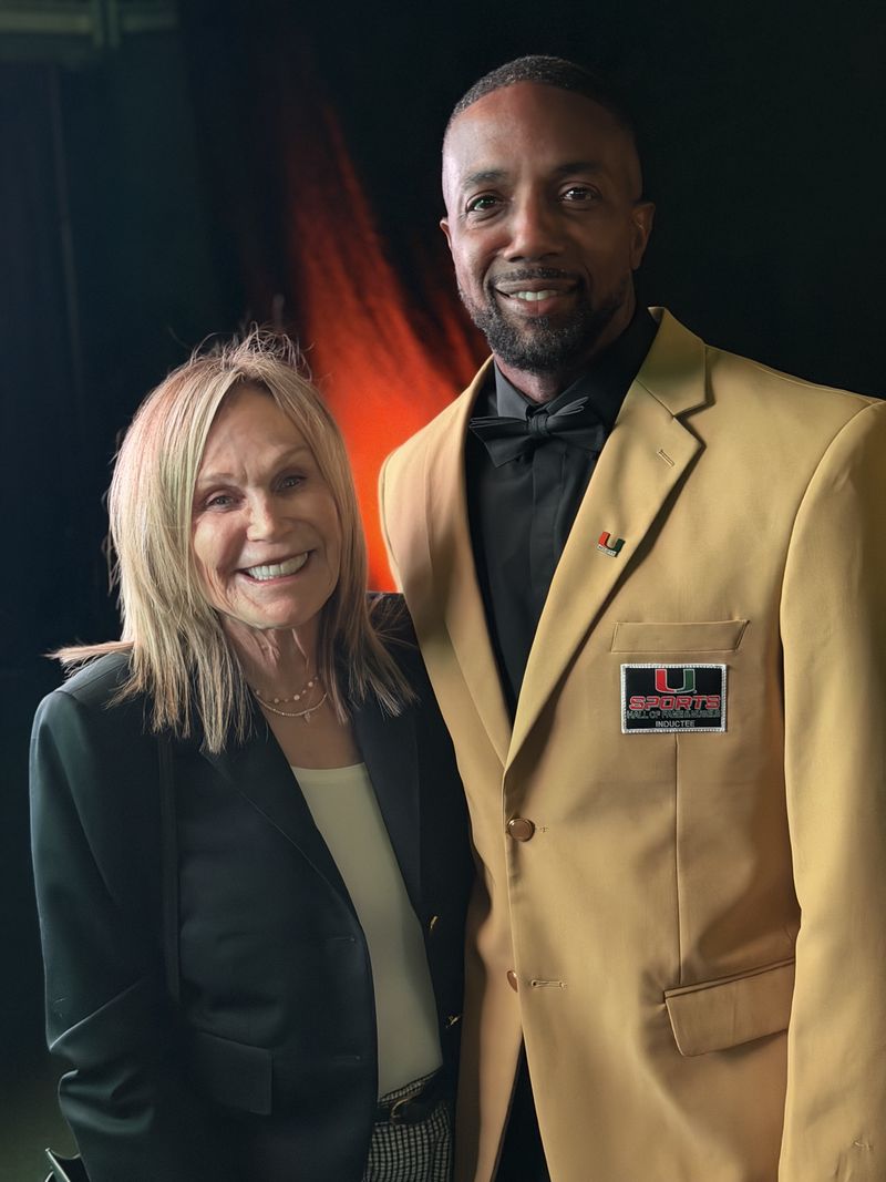 Mike Rumph in his gold UM Sports Hall of Fame inductee jacket, smiling beside a guest