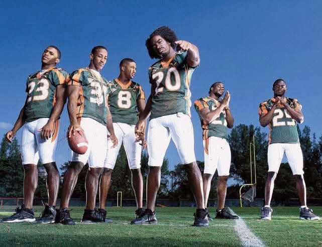 Six Miami Hurricanes players in green and orange jerseys pose on a practice field under a blue sky