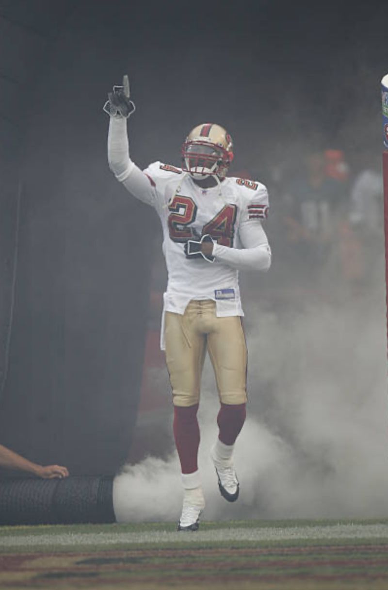 Mike Rumph, number 24, runs out of the tunnel through smoke in the 49ers' white road uniform, pointing one finger up