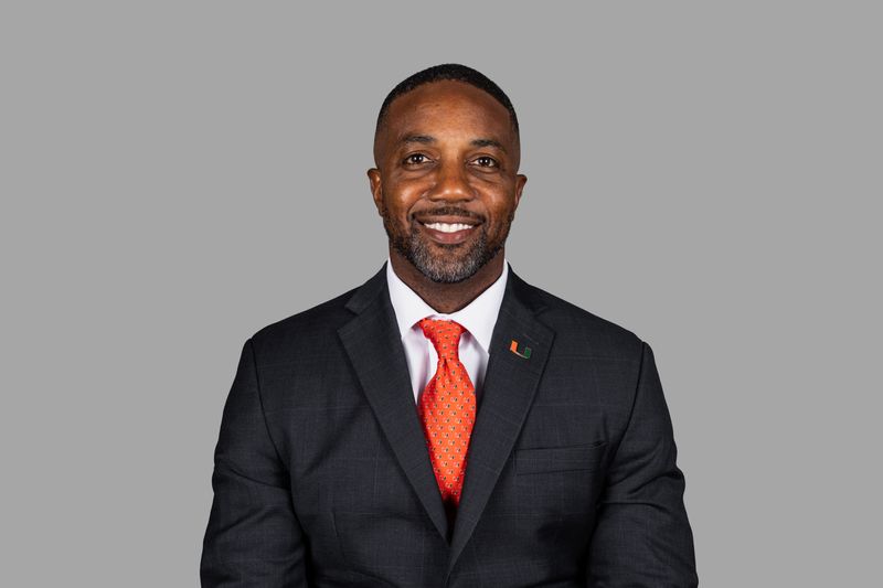 Mike Rumph's University of Miami staff portrait: dark suit, orange tie and a U lapel pin on a gray background